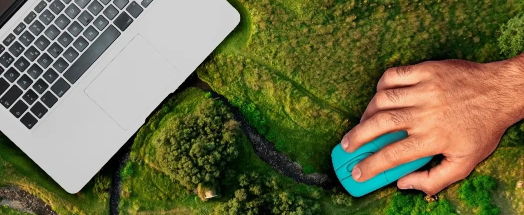 A hand with a mouse operates a laptop for monitoring, reporting, and verification, which is placed on a landscape viewed from above.