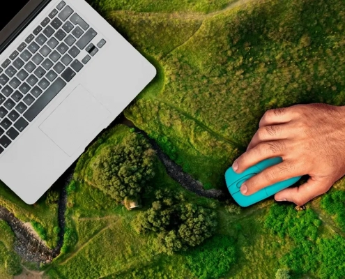A hand with a mouse operates a laptop for monitoring, reporting, and verification, which is placed on a landscape viewed from above.