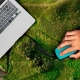 A hand with a mouse operates a laptop for monitoring, reporting, and verification, which is placed on a landscape viewed from above.